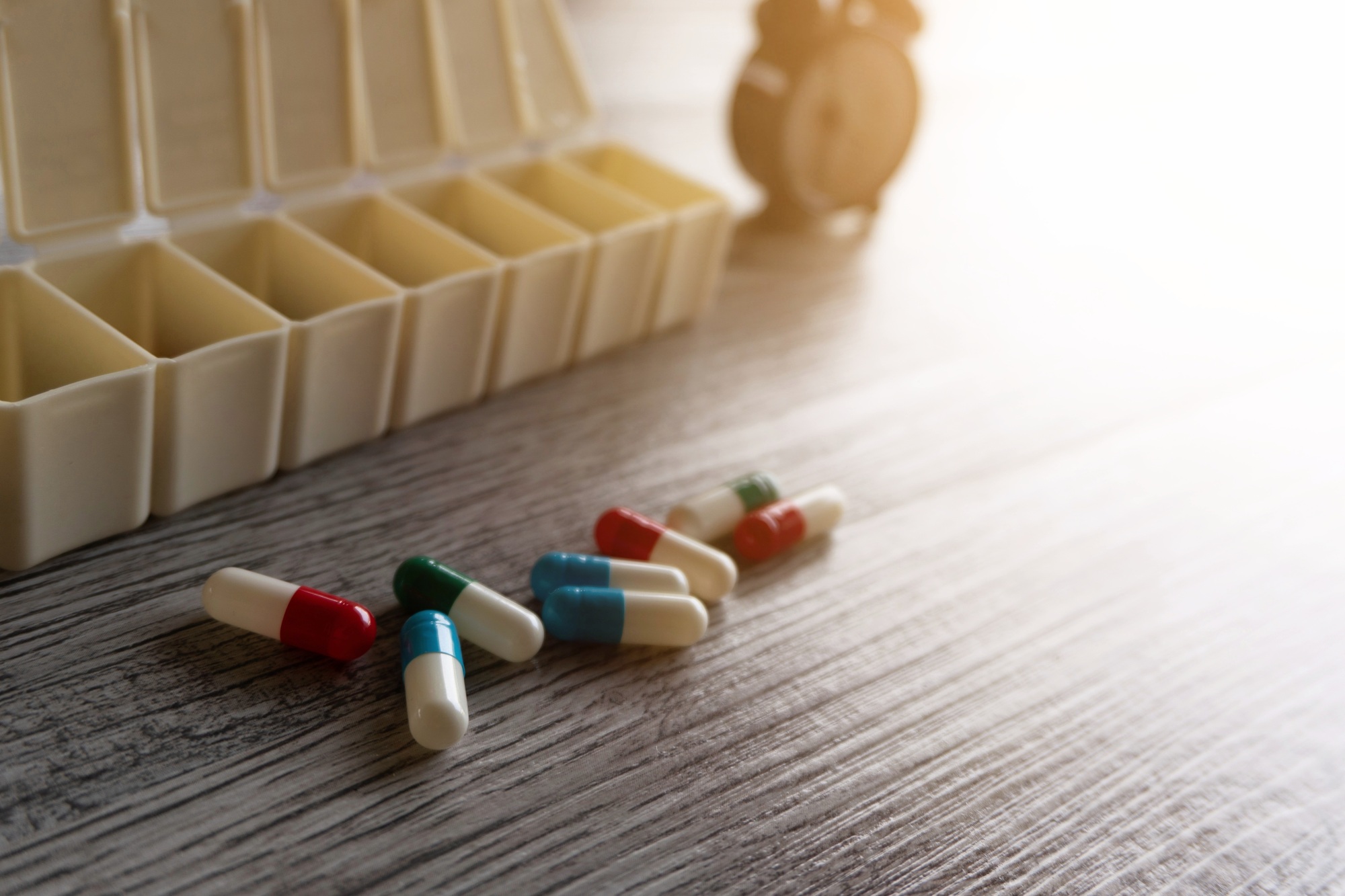 Closeup image of colorful medicine pills, pillbox organizer and alarm clock on table