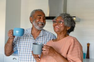 Happy african american senior couple holding mugs with coffee and talking