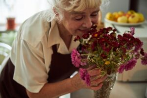 Joyful old woman smelling flowers at home