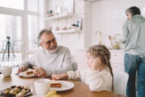 Smiling grandfather and granddaughter eating sandwiches in kitchen